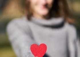 A woman presenting a red heart symbol, showcasing love and compassion.